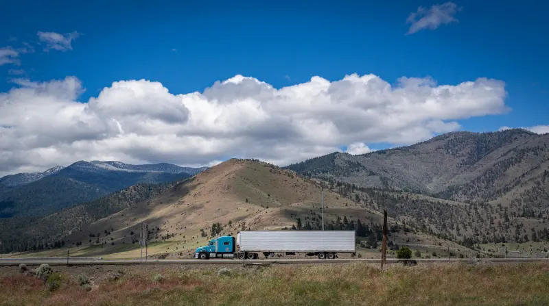 Blue semi truck traveling along a scenic mountain highway