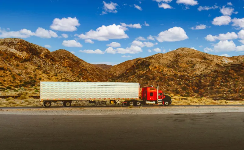 Red semi truck traveling a desert highway with mountain views