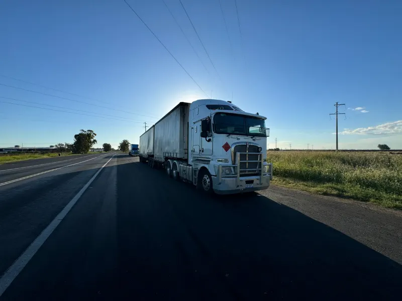 Silver semi truck driving down an open rural highway