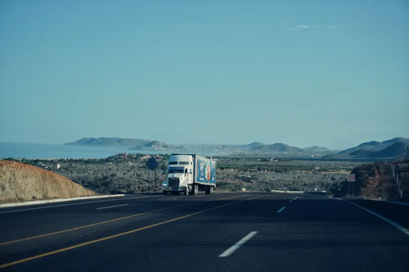Semi-truck traveling a scenic highway with mountains in the background