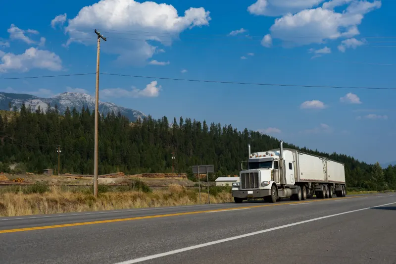 White semi-truck traveling a scenic road with mountains in the background